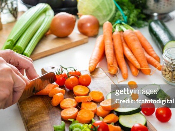 Close up of woman’s hands slicing fresh organic carrots on kitchen counter